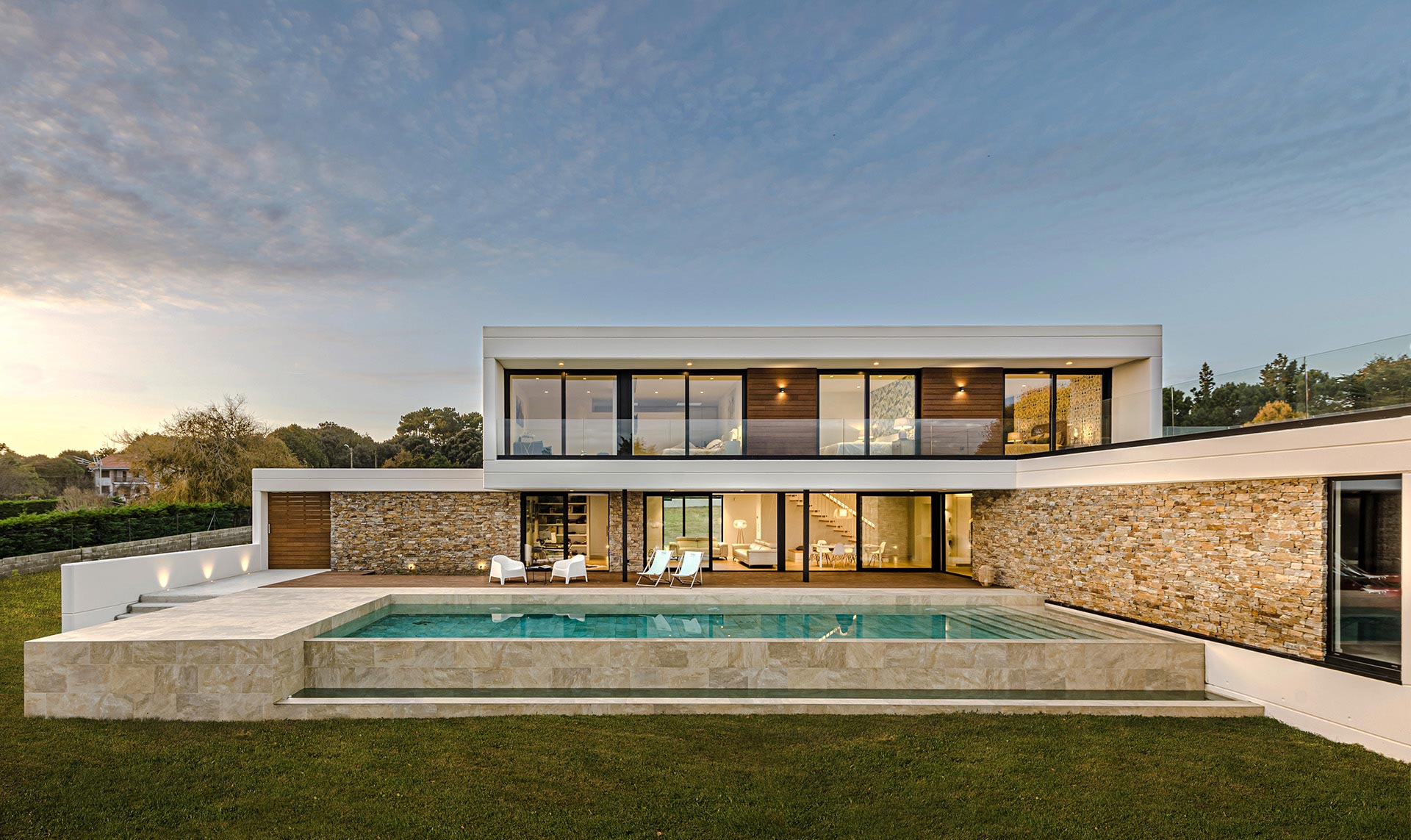 Fachada de vivienda moderna con piscina y grandes cristaleras diseñada por Moah Arquitectos en Loredo