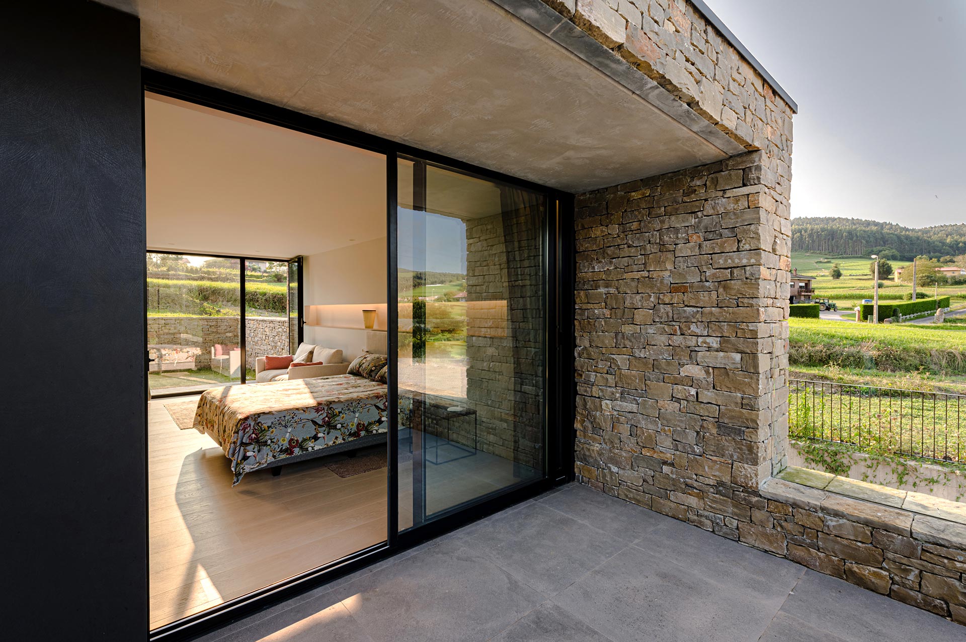 Dormitorio de casa moderna de piedra y grandes cristaleras diseñada por Moah Diseño de Interiores en Cantabria