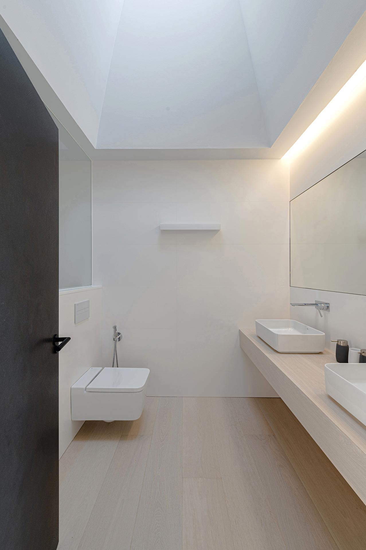 Baño con gres porcelánico blanco y gran lucernario en casa moderna diseñada por Moah Diseño de Interiores en Cantabria
