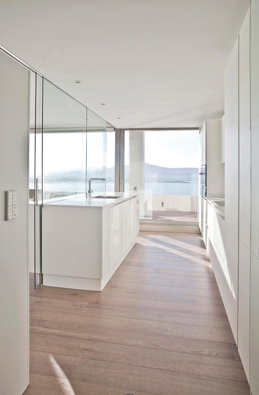 Cocina blanca de diseño con suelo de madera en reforma integral de vivienda diseñada por Moah Arquitectos en Santander