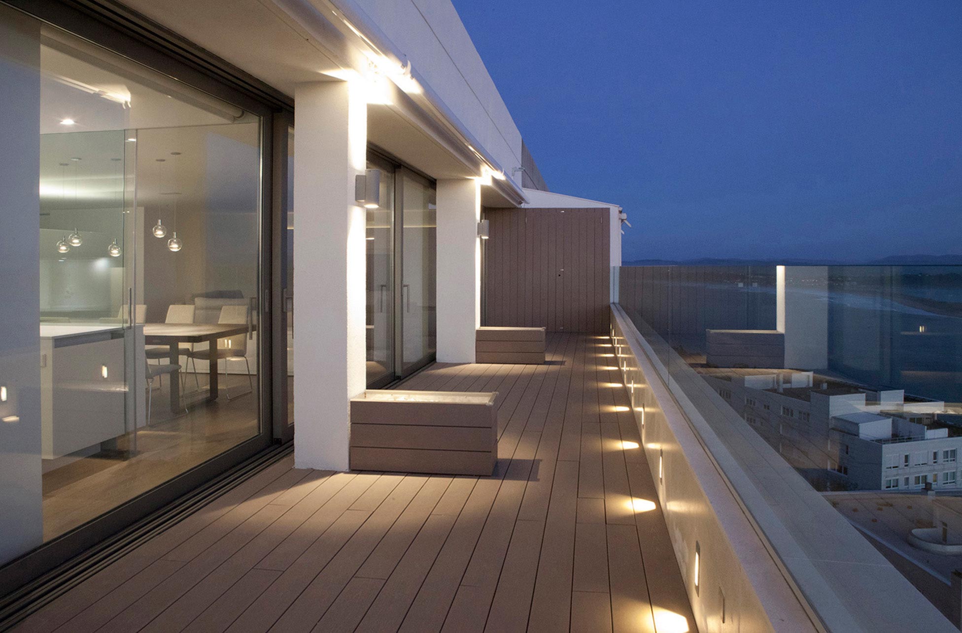 Terraza con iluminación indirecta y madera en reforma integral de piso de lujo diseñada por Moah Diseño de Interiores en Santander