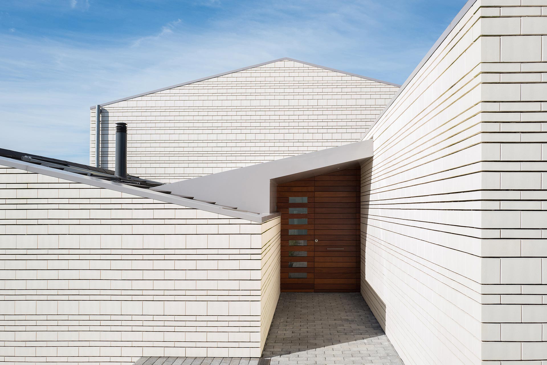 Fachada de ladrillo blanco en casa moderna con cubierta a dos aguas diseñada por Moah Arquitectos en Villaverde, Cantabria