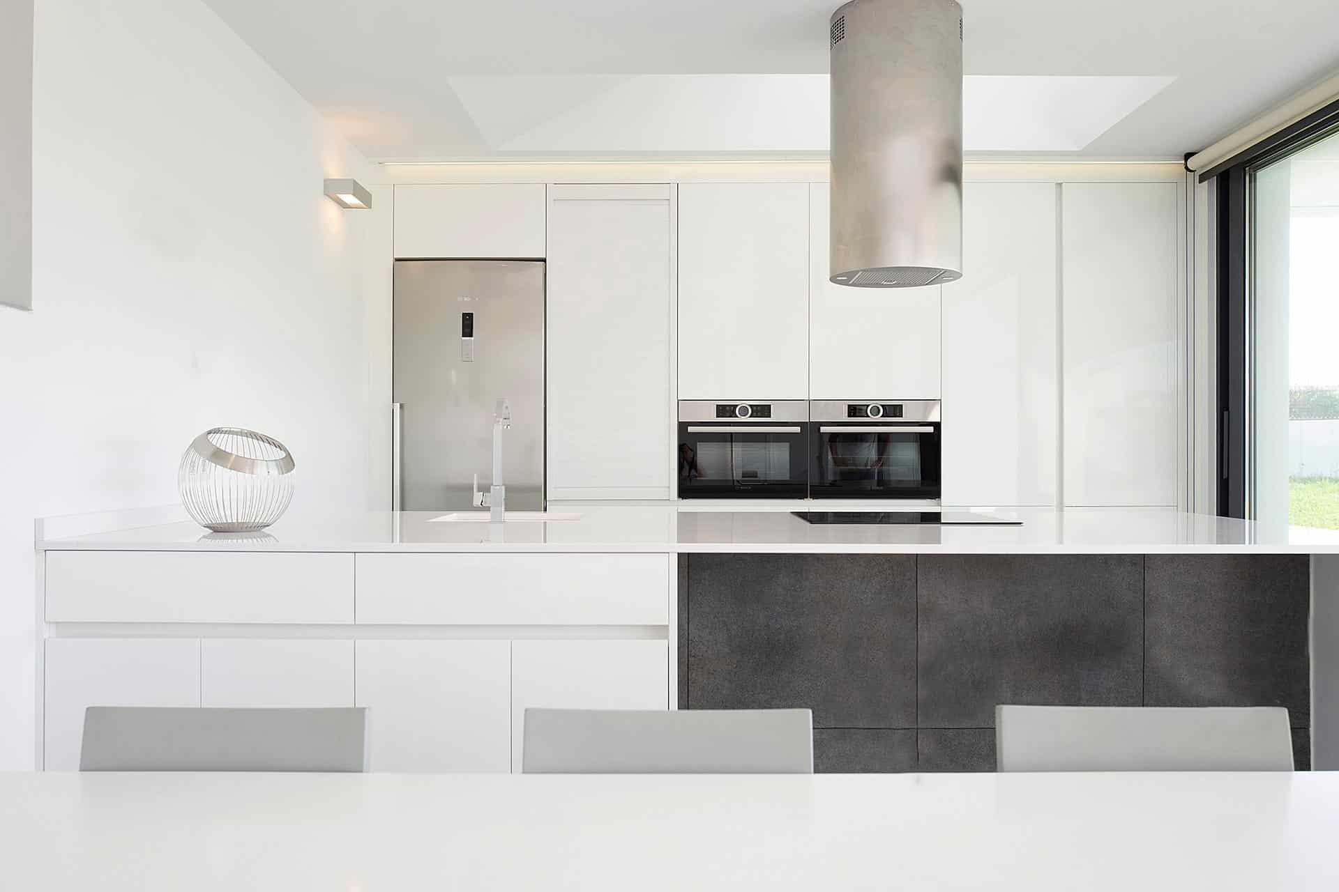 Cocina blanca con isla en casa moderna diseñada por Moah Arquitectos en Villaverde, Cantabria