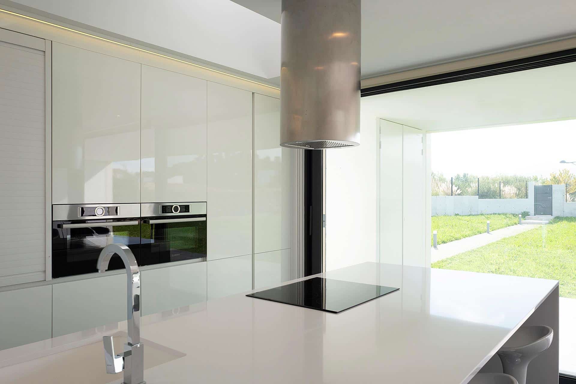 Cocina blanca con isla en casa moderna diseñada por Moah Arquitectos en Villaverde, Cantabria