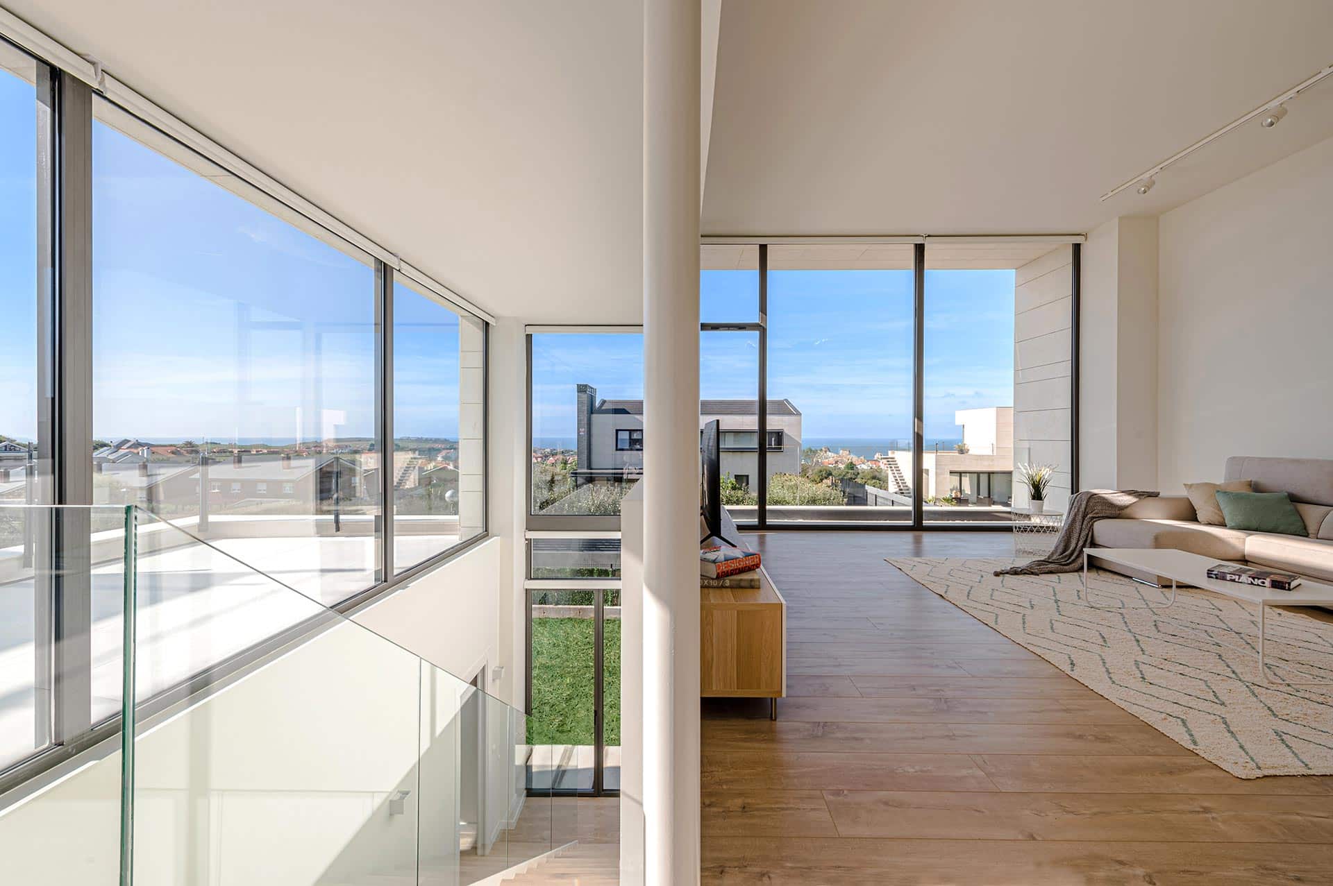 Salón abierto a escalera en casa moderna con grandes cristaleras diseñada por Moah Arquitectos en Liencres. Cantabria