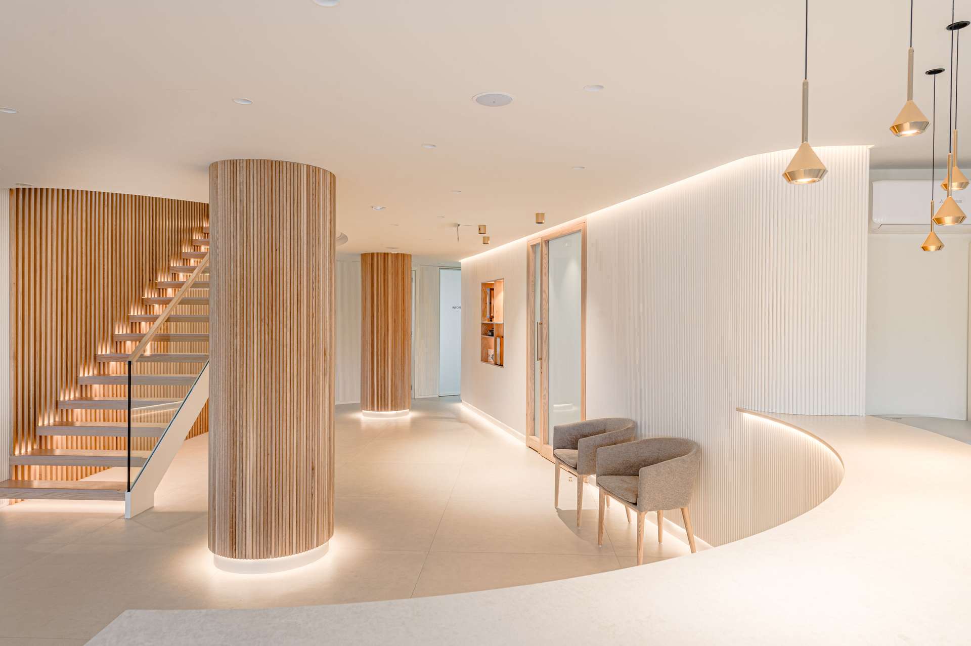 Vestíbulo de entrada con una elegante escalera helicoidal y detalles en madera, concebido por Moah Arquitectos en Santander.