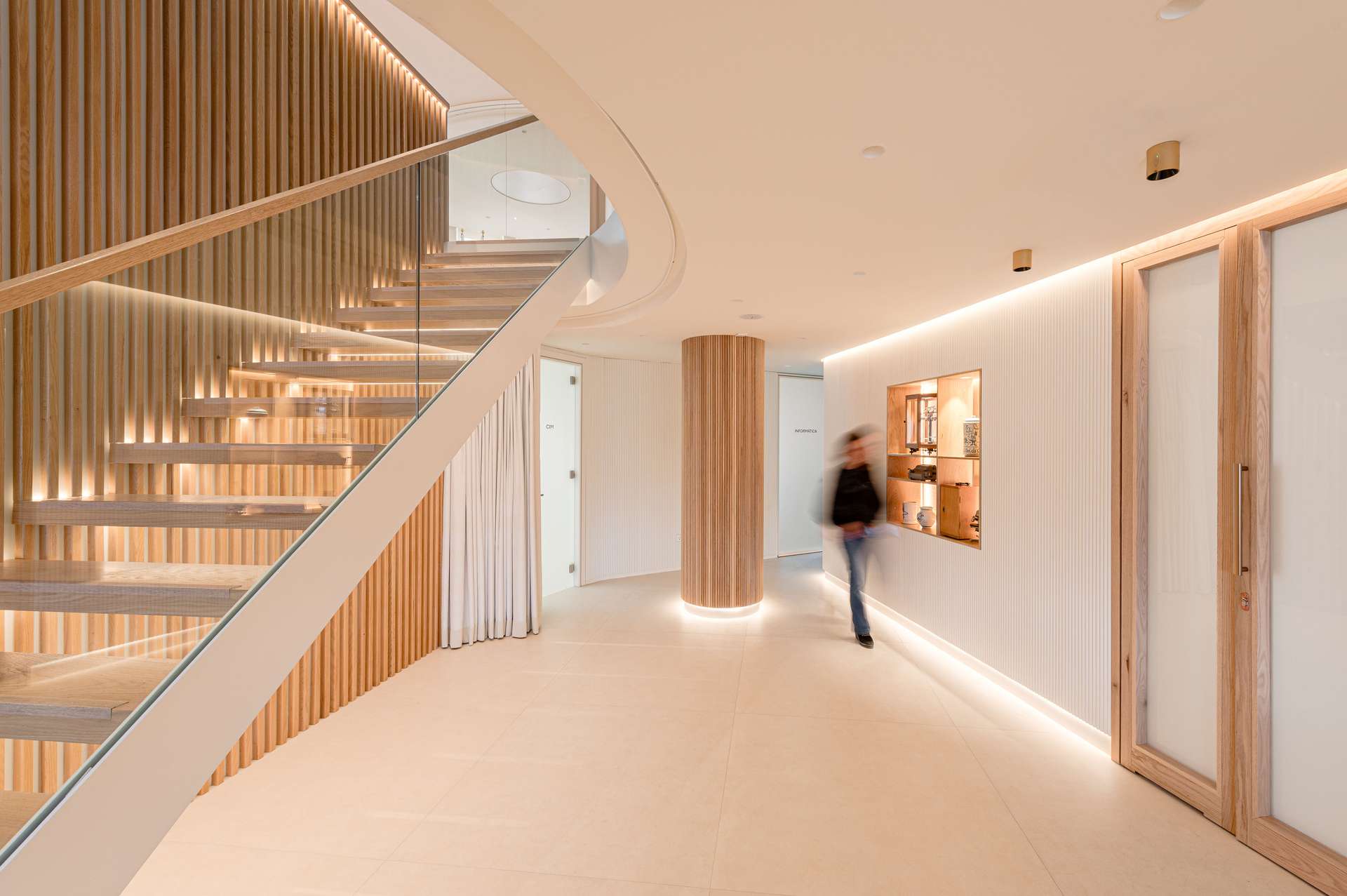 Vestíbulo de entrada con una elegante escalera helicoidal y detalles en madera, diseñada por Moah Arquitectos en Santander.