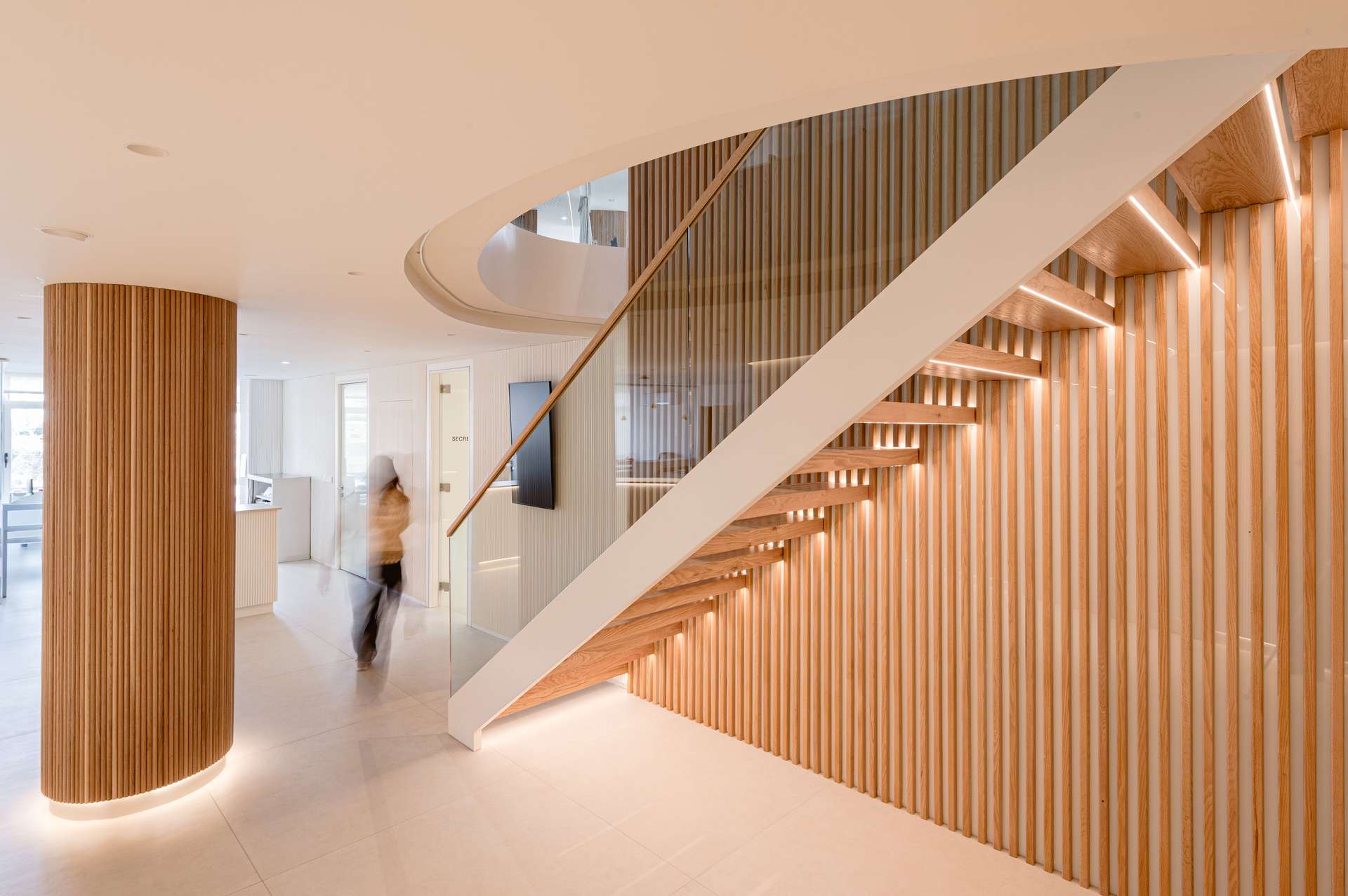 Vestíbulo de entrada con una elegante escalera helicoidal y acabados en madera, diseñada por Moah Arquitectos en Santander.