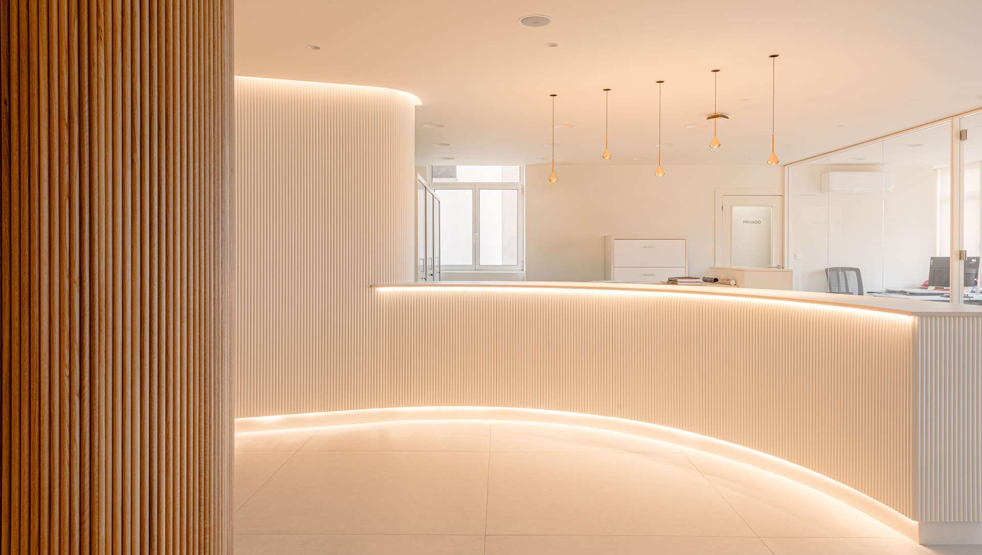 Vestíbulo de entrada con un diseño moderno y luminoso, que incluye una barra de recepción curvada y detalles en madera, diseñada por Moah Arquitectos en Santander.