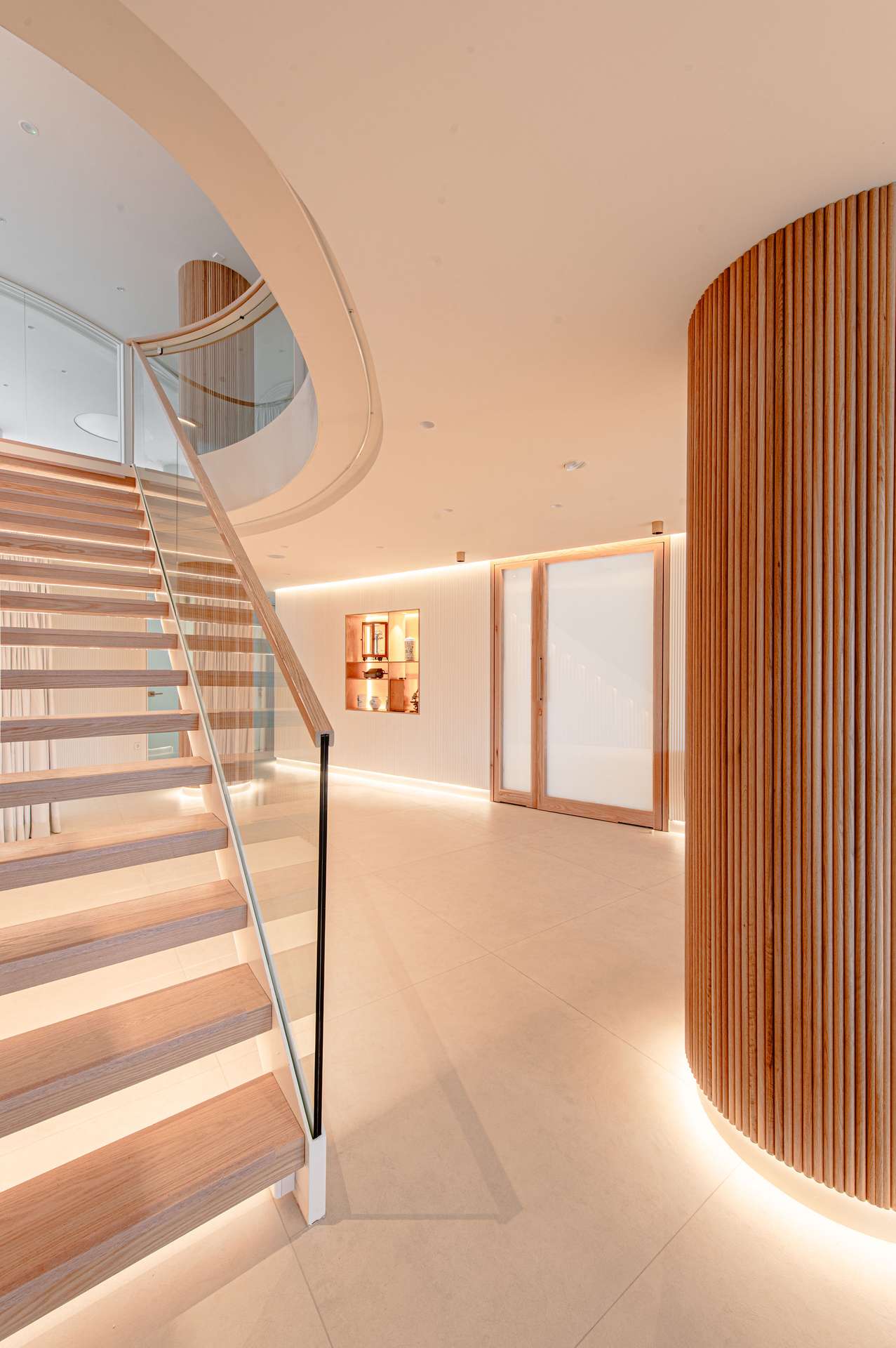 Vestíbulo de entrada con escalera helicoidal y detalles en madera, concebido por Moah Arquitectos en Santander.