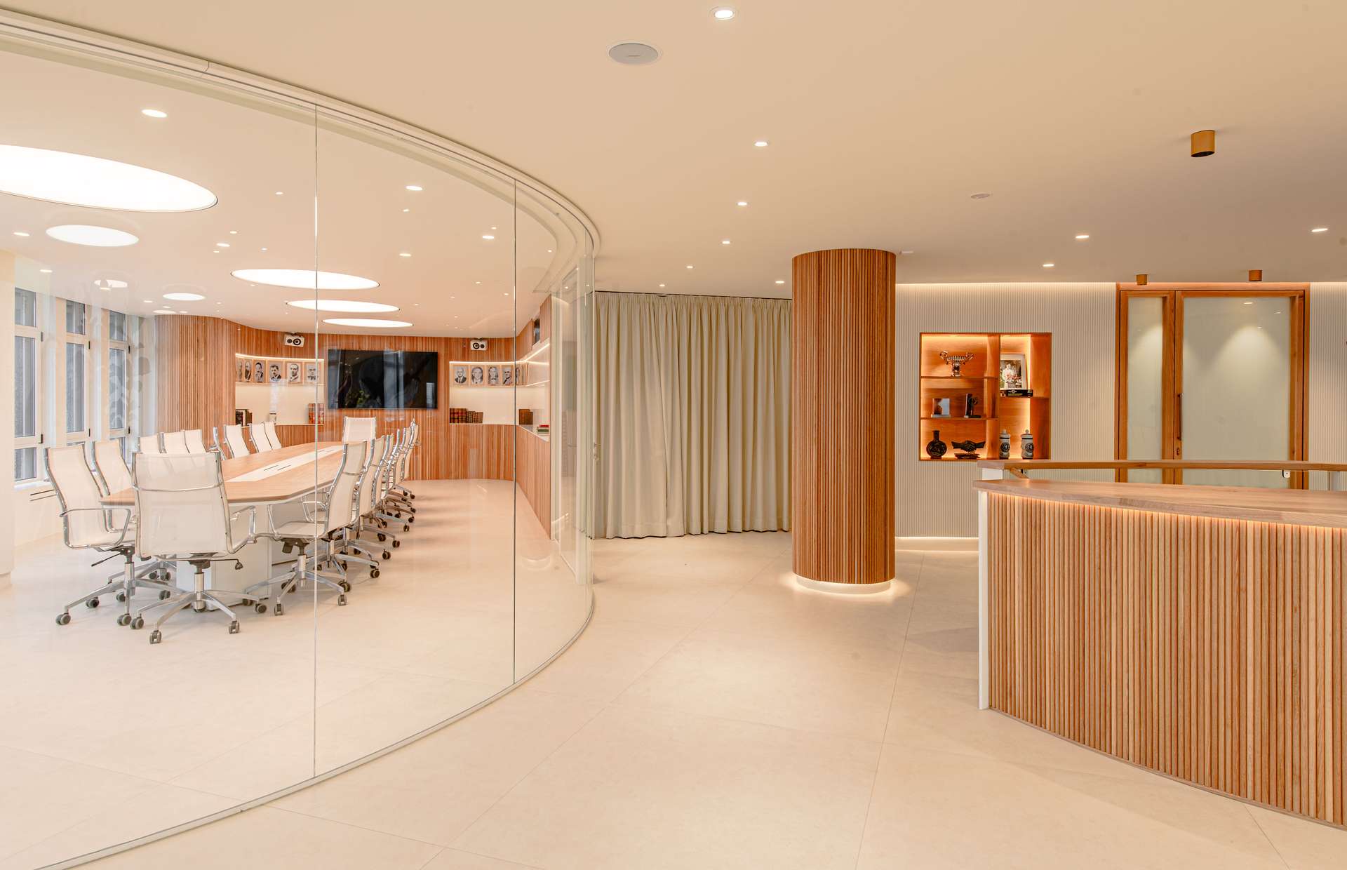 Espacio interior moderno con una mesa de reuniones y sillas blancas, destacando la iluminación y los acabados en madera, concebido por Moah Arquitectos en Santander.