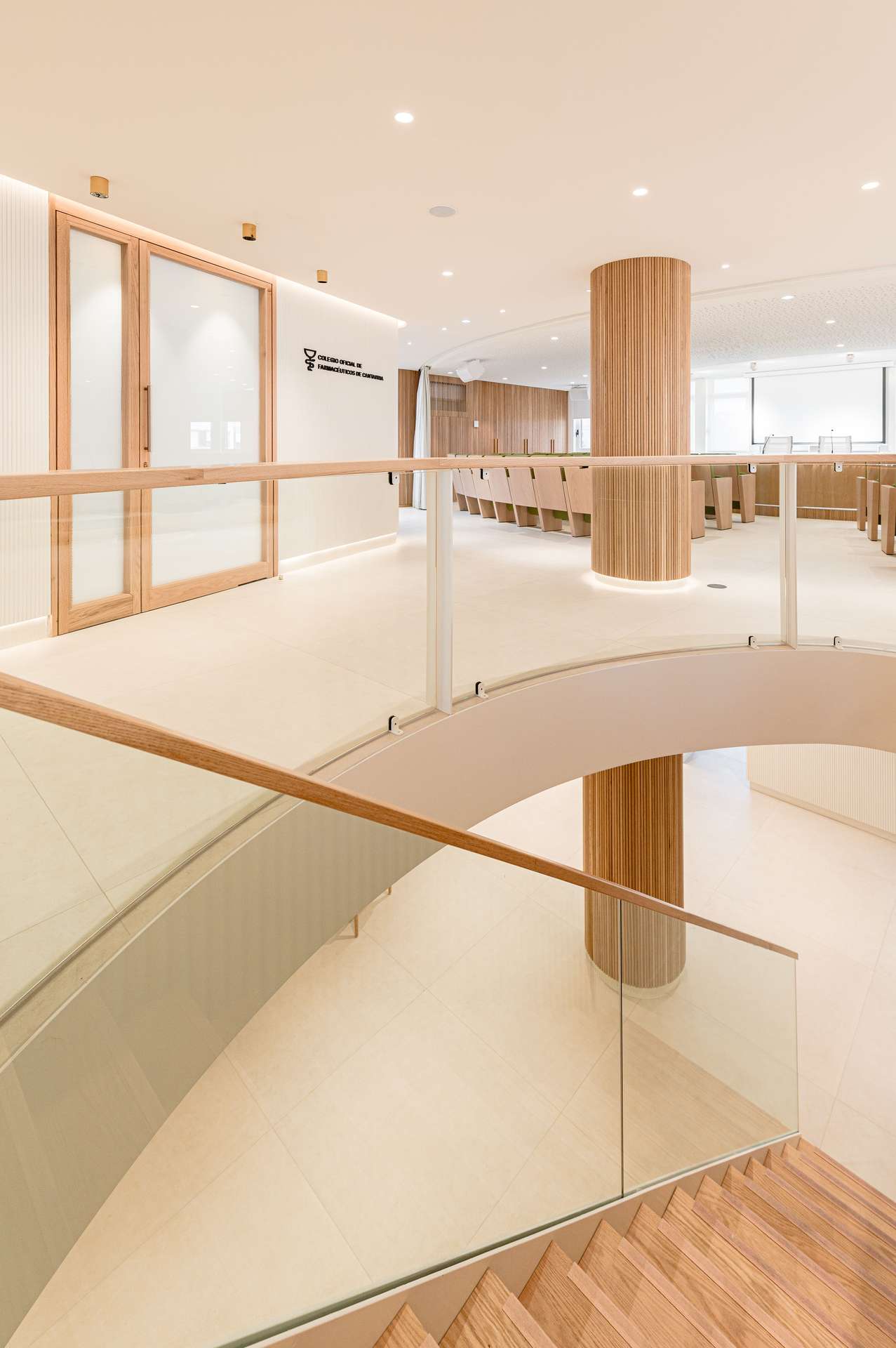 Vestíbulo de entrada con una elegante escalera helicoidal y detalles en madera, concebida por Moah Arquitectos en Santander.