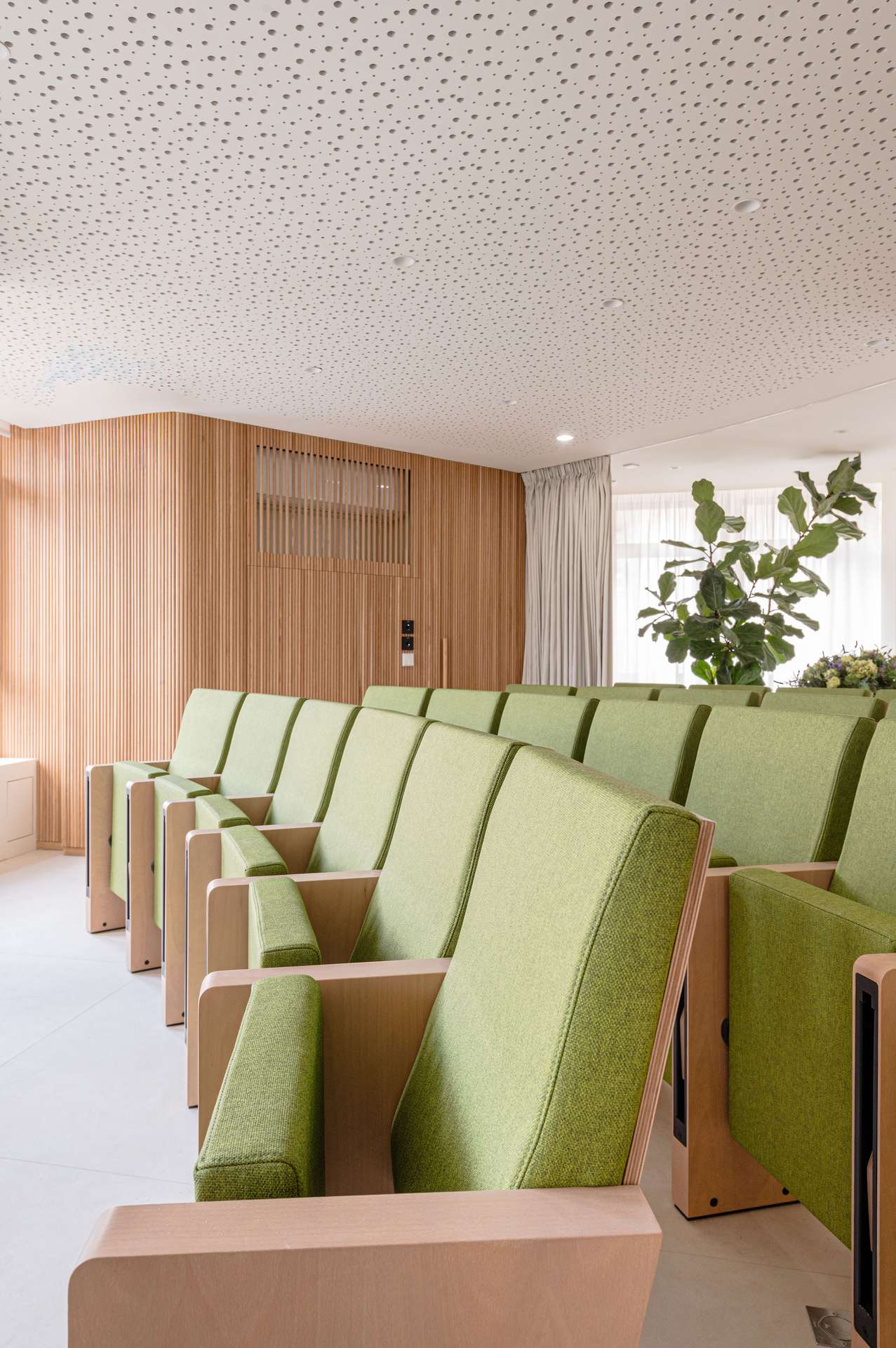 Sala de reuniones con asientos verdes y paneles de madera, diseñada por Moah Arquitectos en Santander.