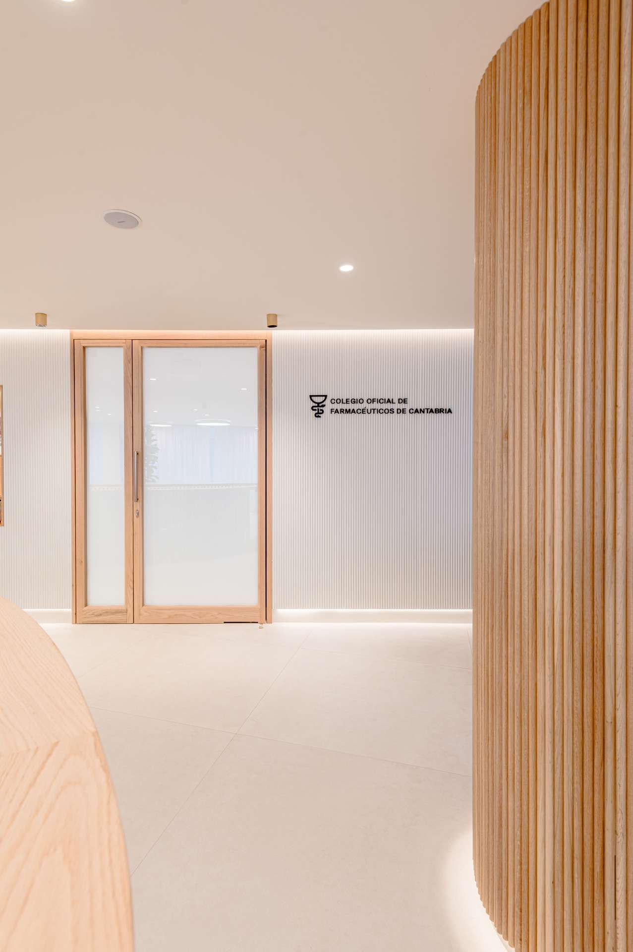 Vestíbulo moderno con acabados en madera y una puerta de cristal, concebido por Moah Arquitectos en Santander.