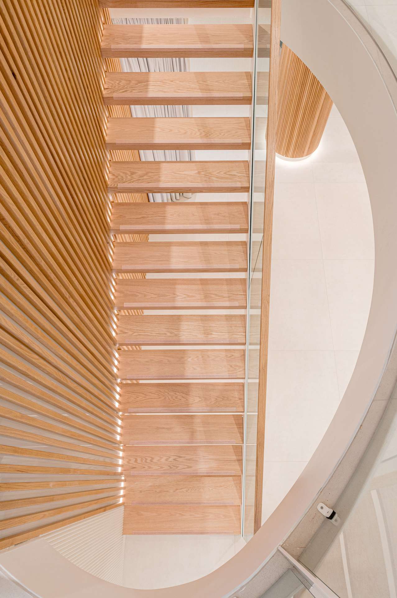 Vista aérea de una elegante escalera helicoidal con peldaños de madera y detalles en paneles de madera, diseñada por Moah Arquitectos en Santander.