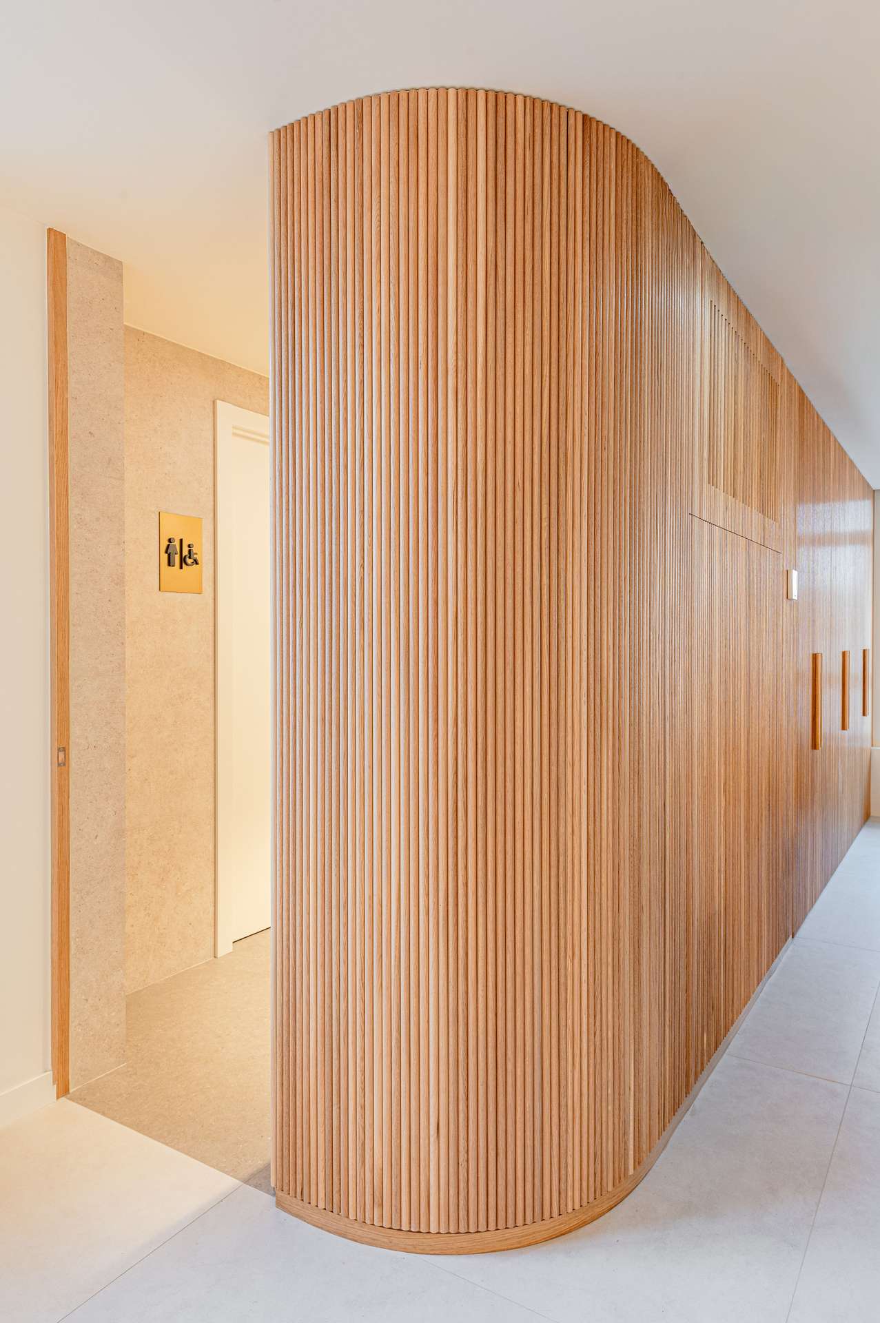 Vista del vestíbulo con un diseño curvado y paneles de madera verticales, concebida por Moah Arquitectos en Santander.