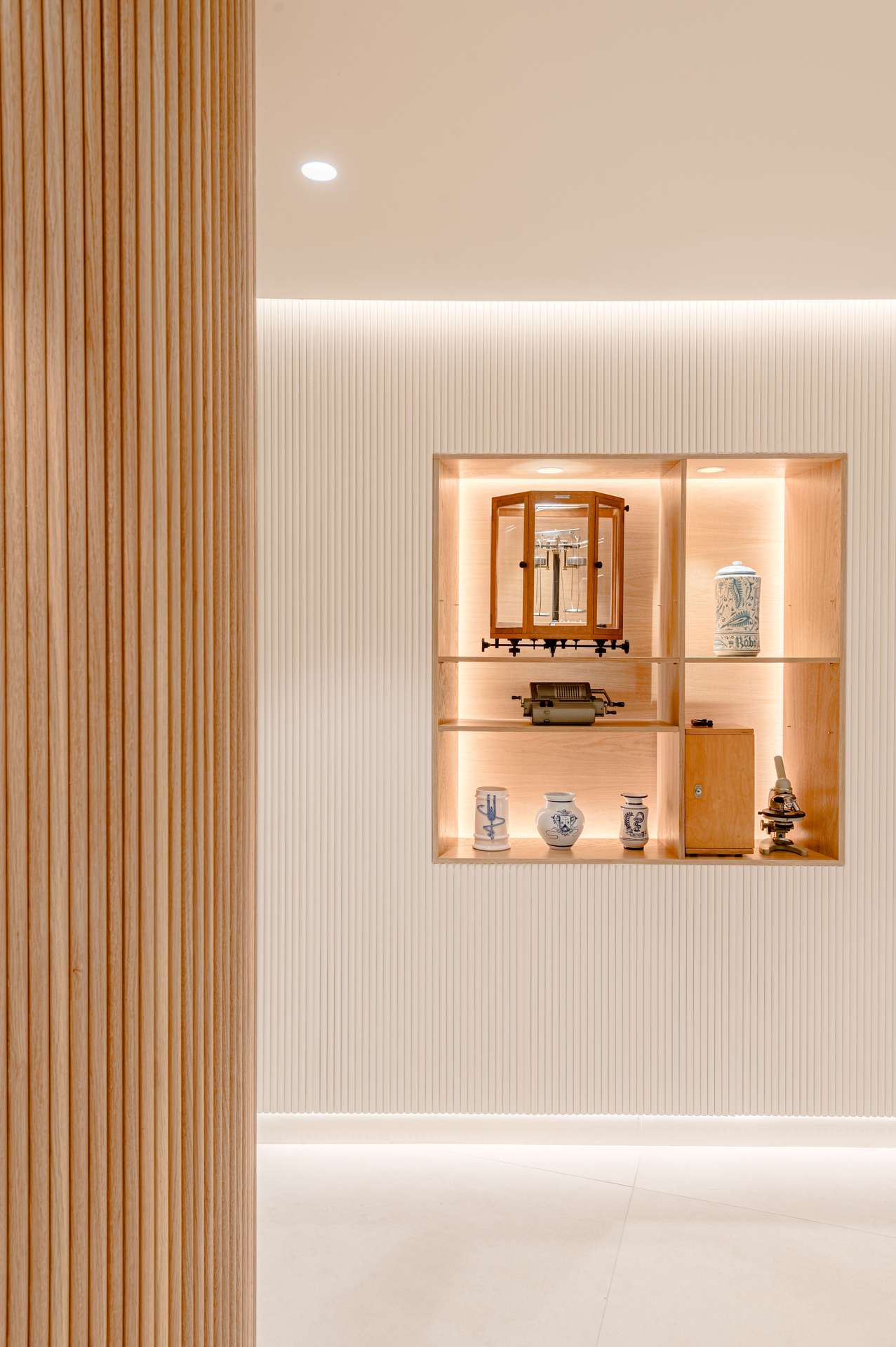 Interior moderno con paneles de madera y estantería iluminada que exhibe objetos históricos, diseñada por Moah Arquitectos en Santander.
