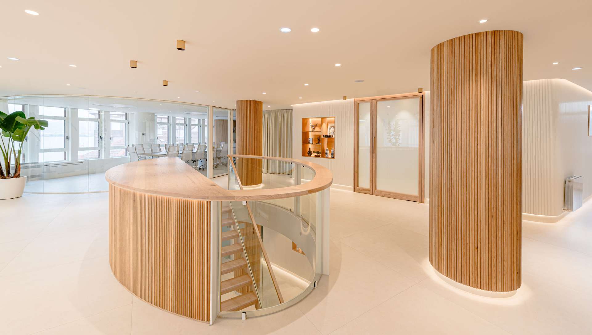 Vestíbulo de entrada con una elegante escalera helicoidal y acabados en madera, diseñada por Moah Arquitectos en Santander.