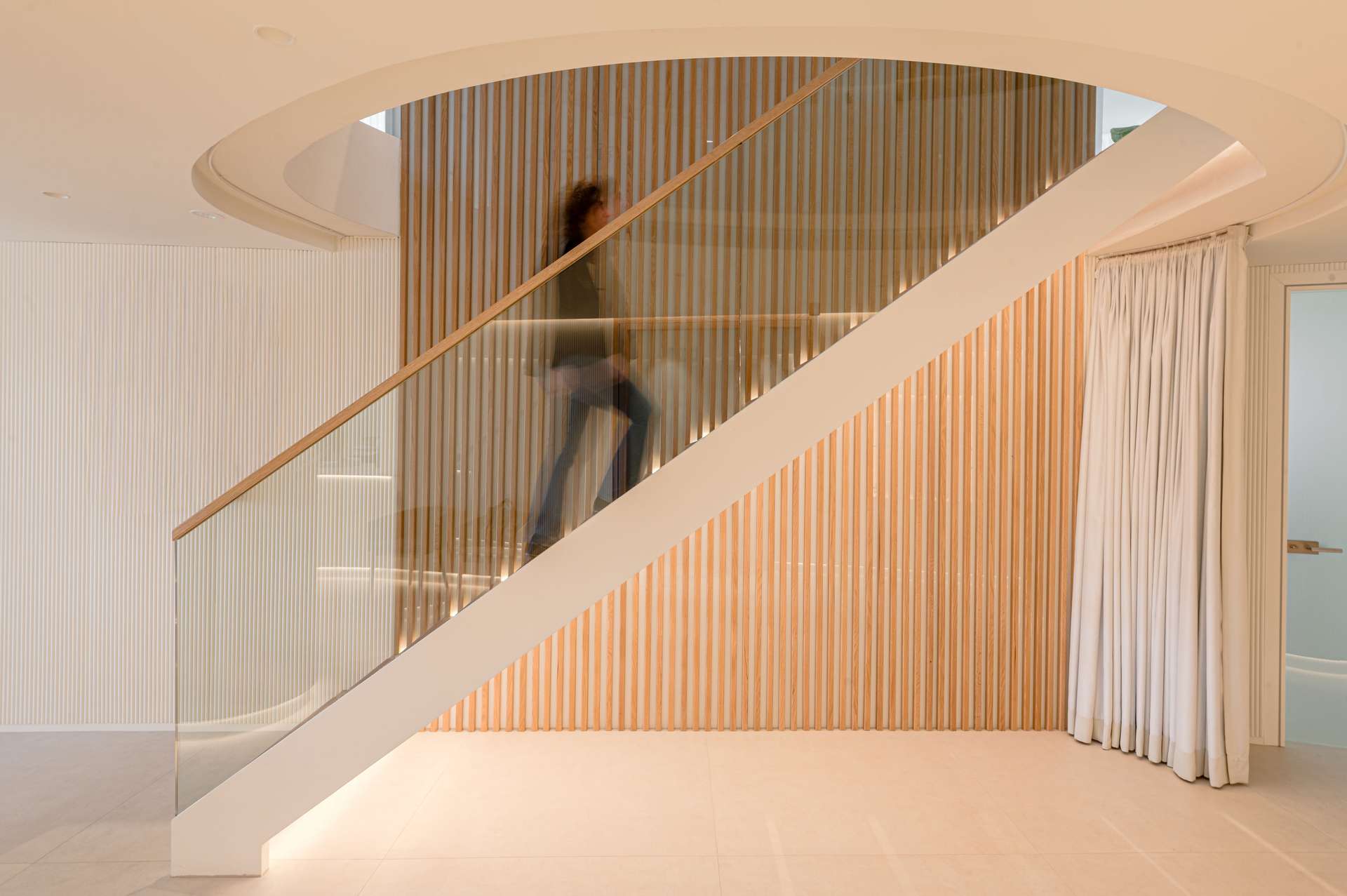 Vestíbulo de entrada con una elegante escalera helicoidal y paneles de madera, diseñada por Moah Arquitectos en Santander.